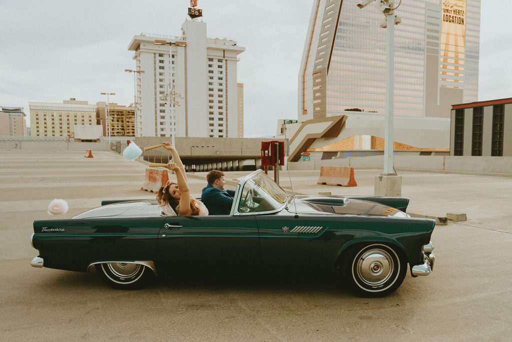 Couple rides off in vintage blue car with their cotton candy flying behind them while they have fun at their street elopement in Las Vegas