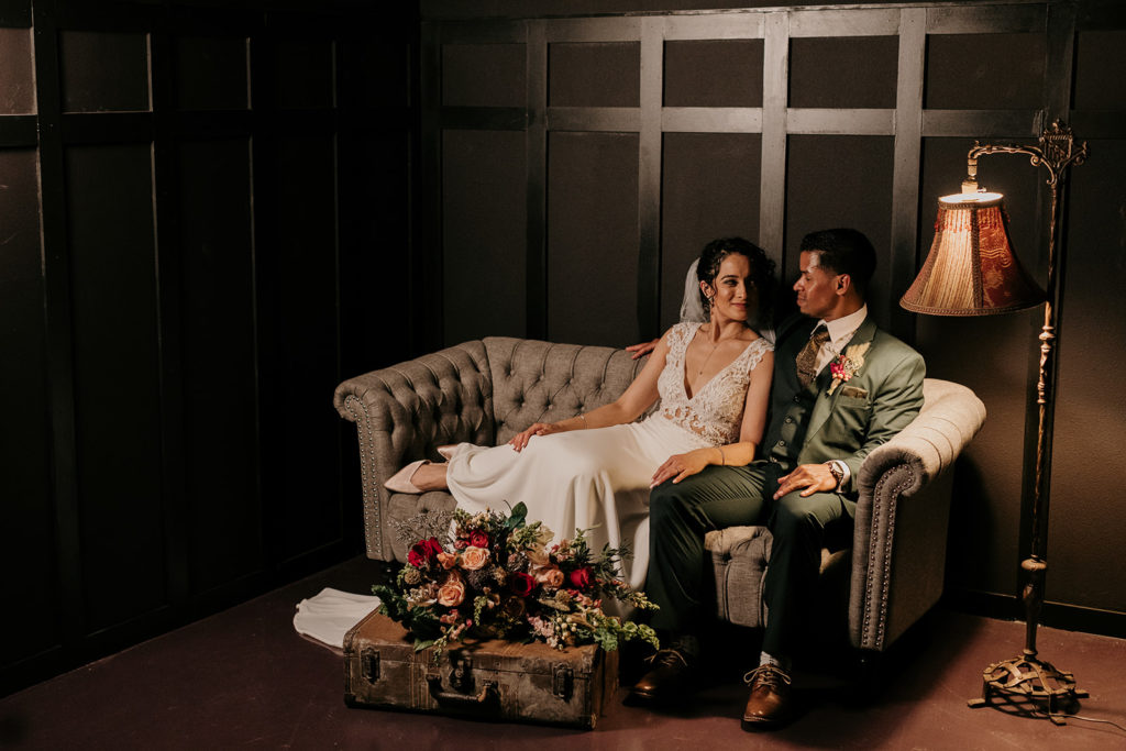 bride and groom in black room with lamp in lounge chair