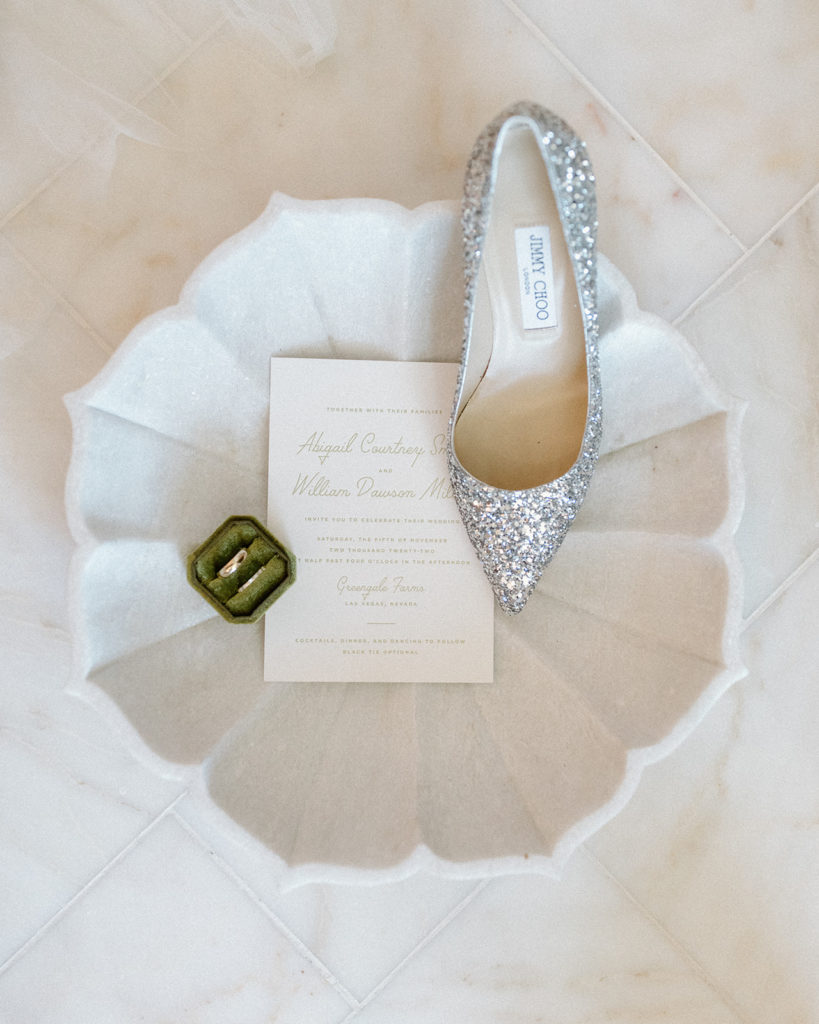 flatlay of shoe, ring box, and wedding invite