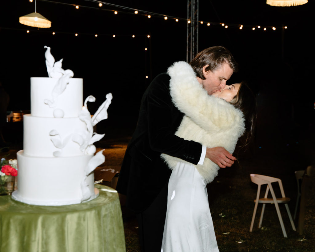 bride and groom kiss in front of boujee wedding cake