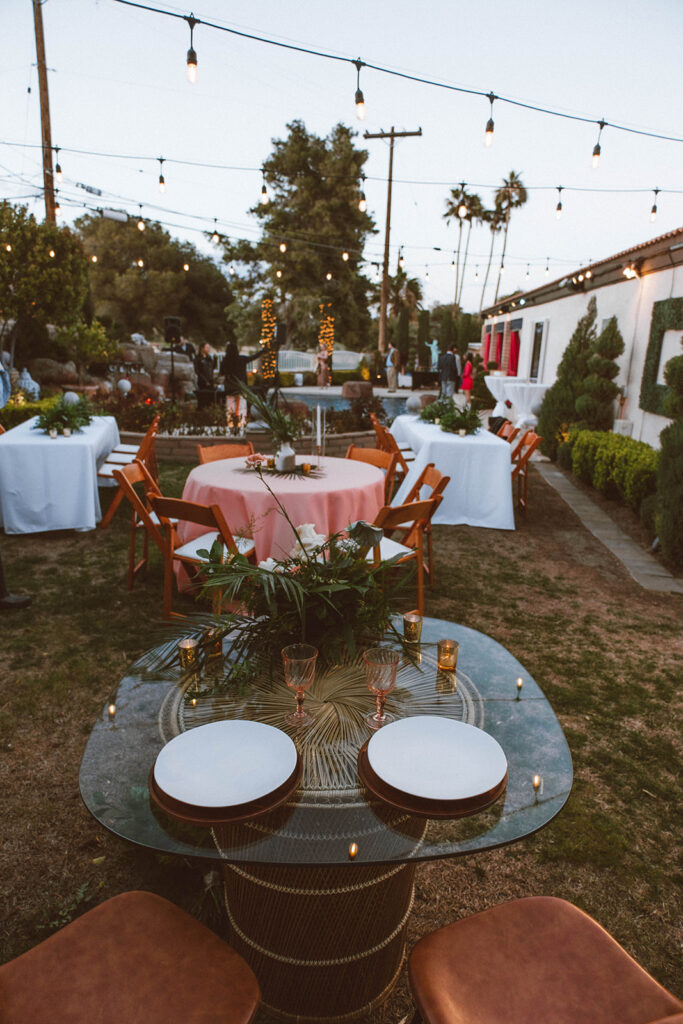 view from the sweetheart table. Palm springs chic inspired orange velvet chairs, white and pink tablecloths and greenery centerpieces and mismatched candles