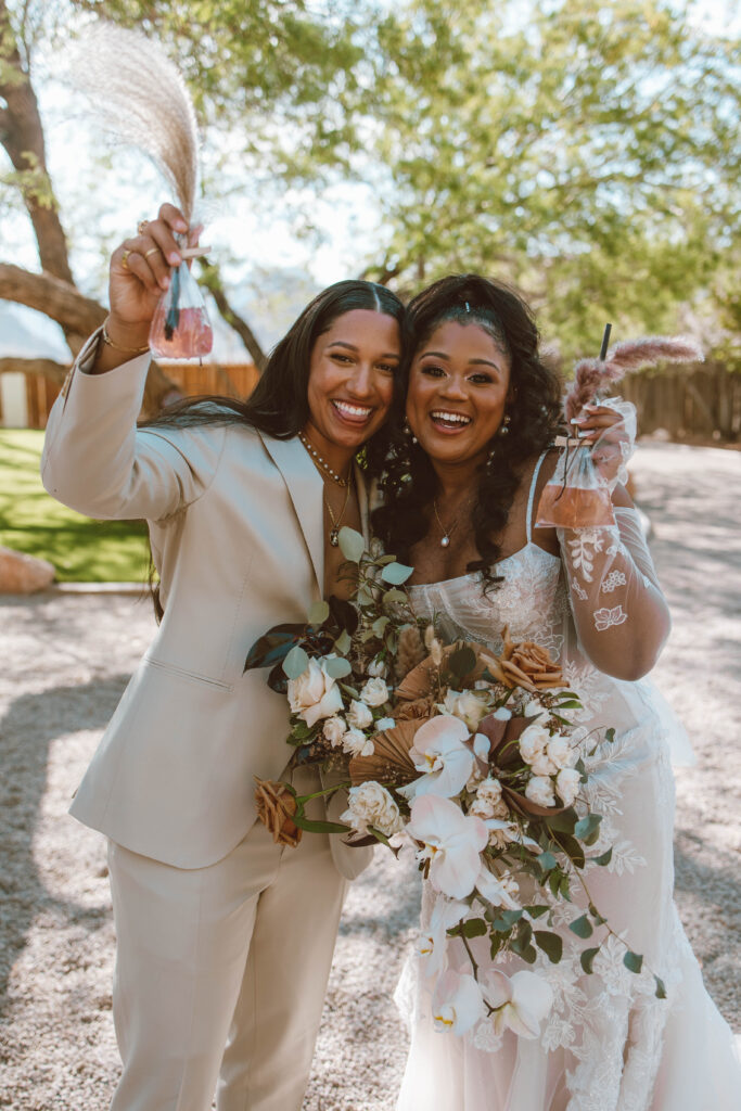 brides Kia and Q, pose with alcoholic boho bags at their garden chic wedding