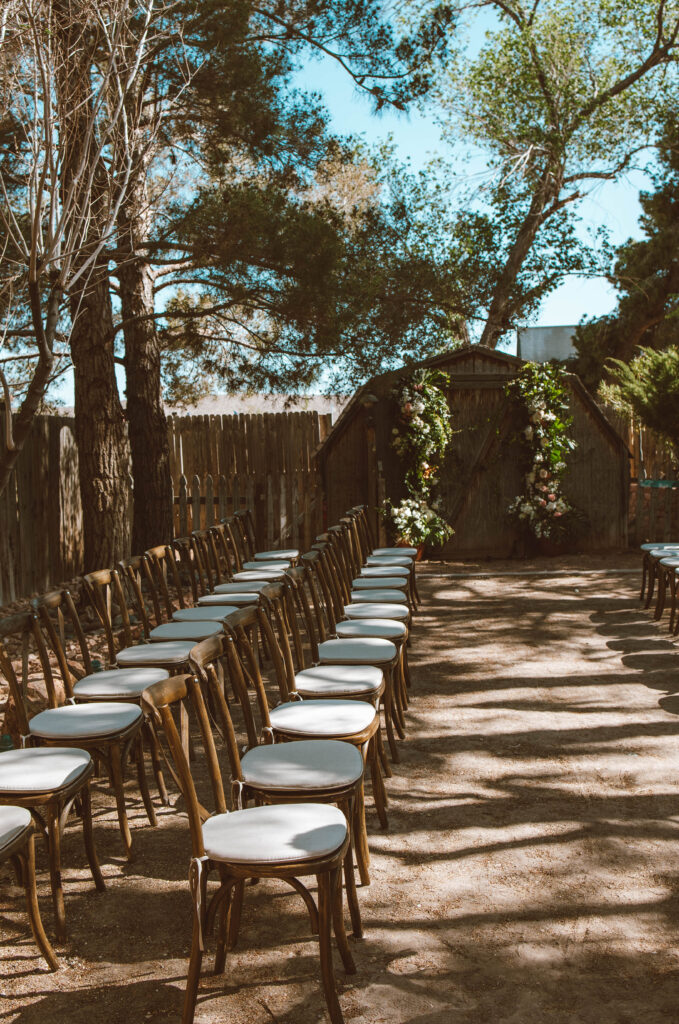 garden chic runway aisle set-up of wooden chairs with white cushions on dirt ground
