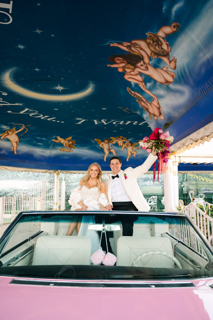 Johnny and Kolby raising their bouquets in a pink Cadillac inside the Tunnel of Love at A Little White Wedding Chapel